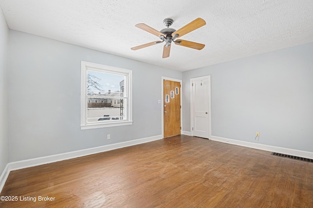 unfurnished room with a textured ceiling, wood finished floors, a ceiling fan, visible vents, and baseboards