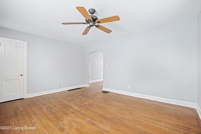 empty room featuring arched walkways, baseboards, and light wood-style floors