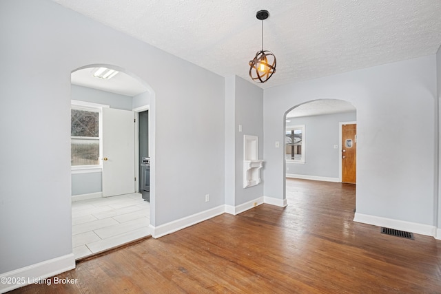 unfurnished room featuring arched walkways, a textured ceiling, and wood finished floors