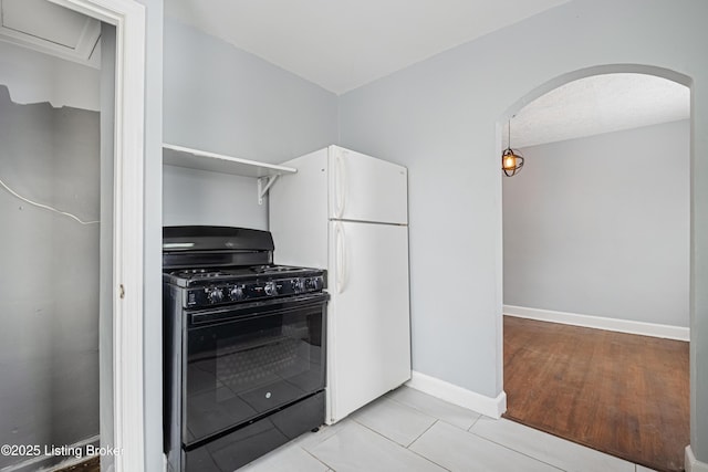 kitchen featuring arched walkways, freestanding refrigerator, black gas stove, a textured ceiling, and baseboards