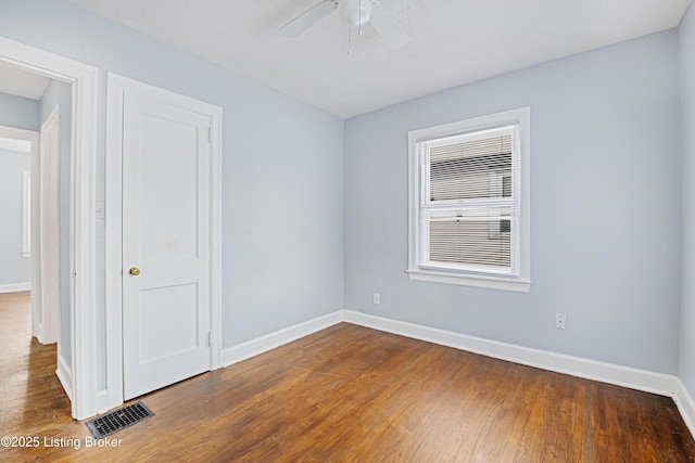 unfurnished room featuring a ceiling fan, baseboards, visible vents, and wood finished floors