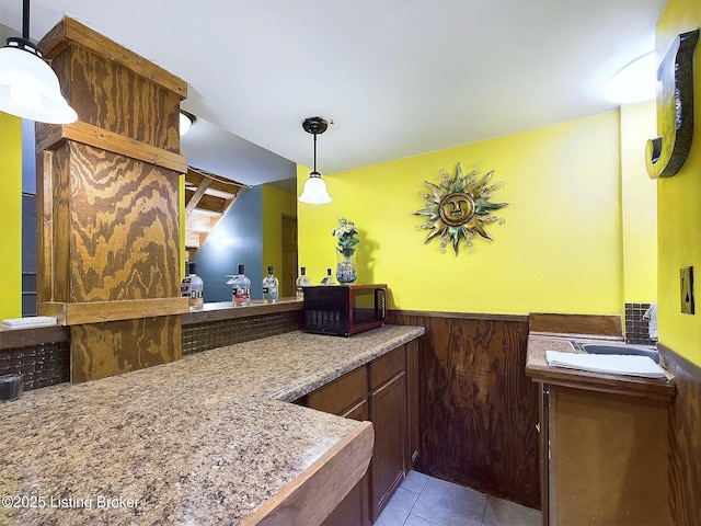 kitchen with black microwave, wainscoting, hanging light fixtures, and light tile patterned flooring