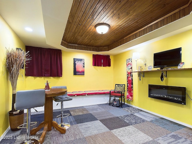 rec room with a tray ceiling, a glass covered fireplace, wood ceiling, and baseboards