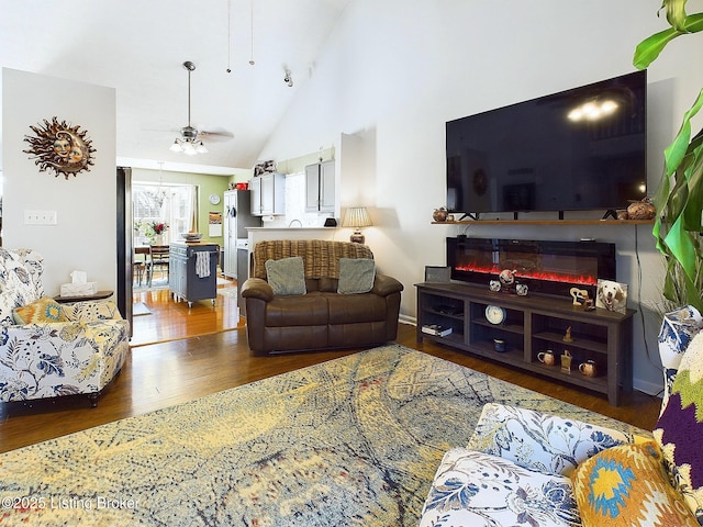 living area with ceiling fan, high vaulted ceiling, wood finished floors, and a glass covered fireplace