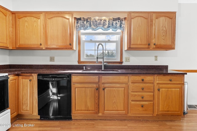 kitchen featuring light wood finished floors, black dishwasher, dark stone counters, and a sink