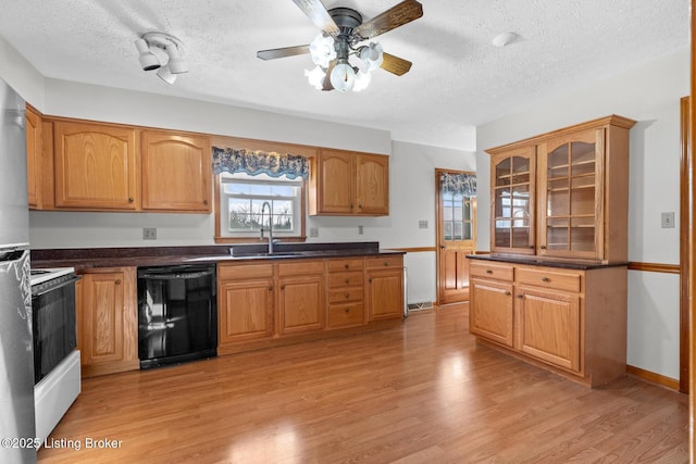 kitchen with light wood-style flooring, a sink, dishwasher, dark countertops, and glass insert cabinets