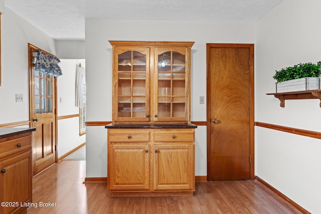 kitchen featuring a textured ceiling, light wood-type flooring, and glass insert cabinets