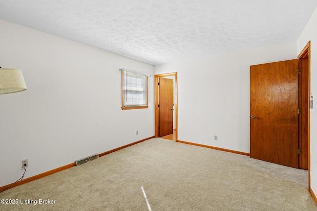 carpeted spare room with a textured ceiling, visible vents, and baseboards