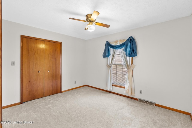 unfurnished bedroom featuring carpet floors, a closet, visible vents, a ceiling fan, and baseboards