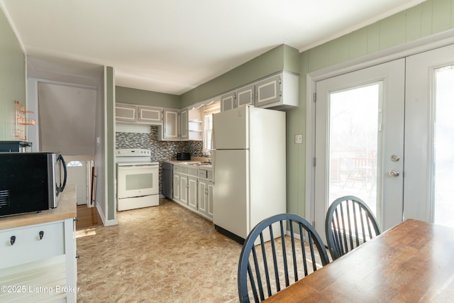 kitchen featuring light countertops, backsplash, a sink, white appliances, and plenty of natural light