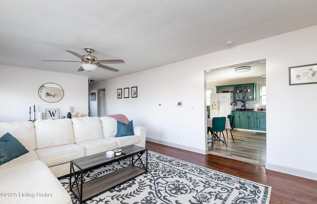 living room featuring ceiling fan, baseboards, and dark wood finished floors