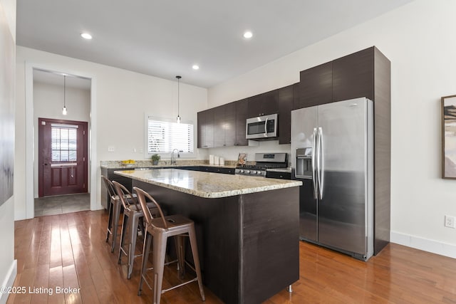 kitchen featuring pendant lighting, appliances with stainless steel finishes, light wood-style floors, a kitchen island, and a kitchen bar