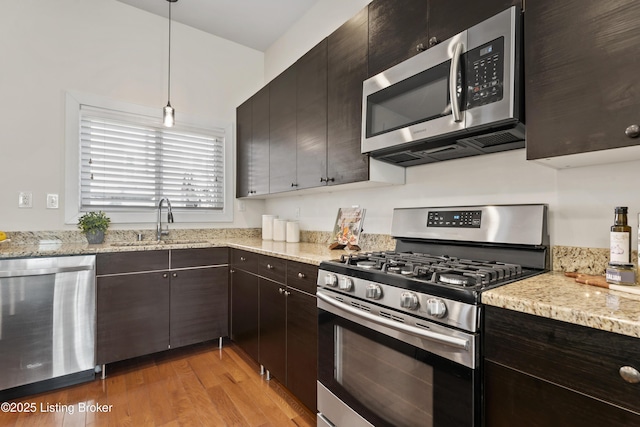 kitchen featuring light wood finished floors, dark brown cabinetry, appliances with stainless steel finishes, hanging light fixtures, and a sink