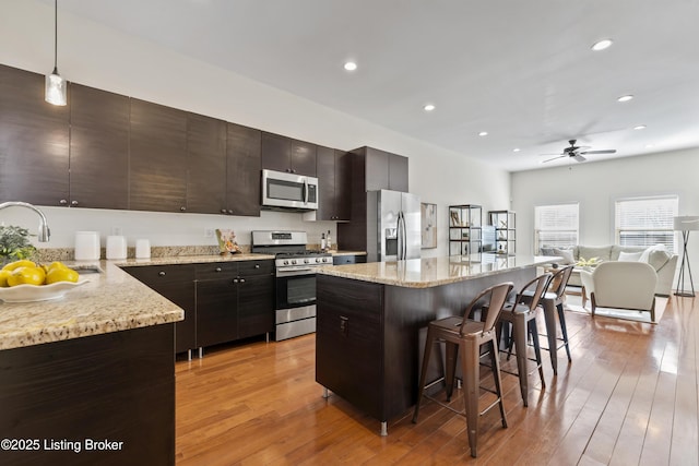 kitchen featuring stainless steel appliances, a kitchen island, a sink, open floor plan, and decorative light fixtures