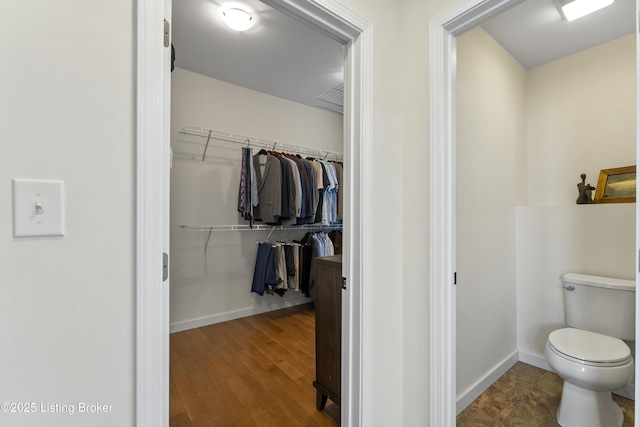 bathroom featuring toilet, baseboards, a walk in closet, and wood finished floors