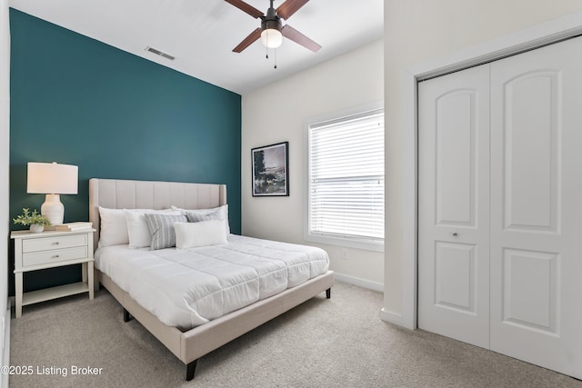 bedroom with a closet, light colored carpet, visible vents, a ceiling fan, and baseboards