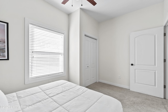 bedroom featuring baseboards, a closet, a ceiling fan, and light colored carpet