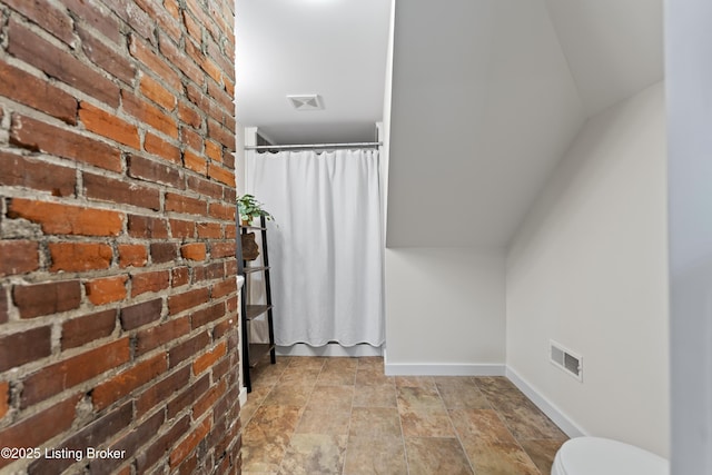 bathroom featuring baseboards, visible vents, toilet, and brick wall