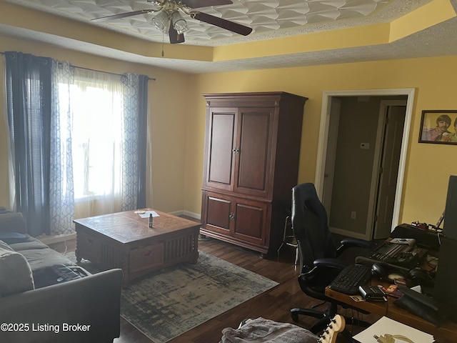 office with dark wood-style floors, a raised ceiling, and a healthy amount of sunlight