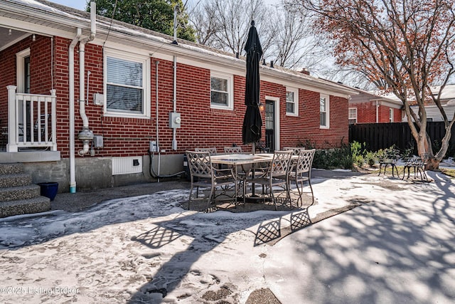 snow covered house with outdoor dining space, a patio area, brick siding, and fence