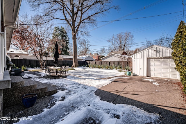 yard covered in snow with driveway, a garage, fence, and an outbuilding