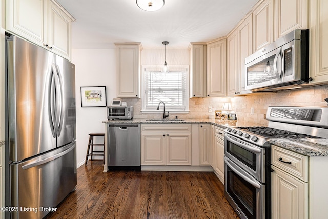 kitchen with cream cabinetry, decorative light fixtures, appliances with stainless steel finishes, a sink, and light stone countertops