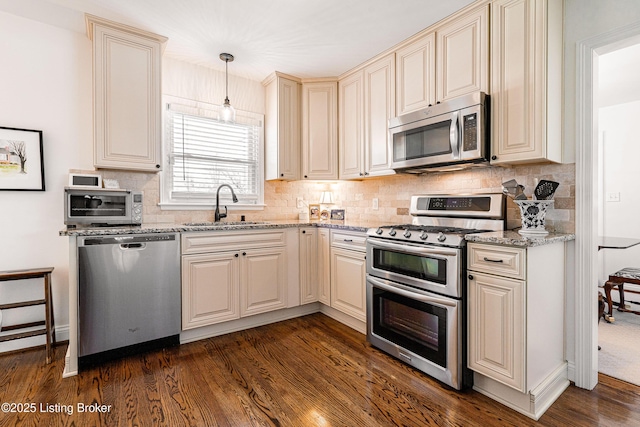 kitchen with appliances with stainless steel finishes, a sink, light stone counters, and pendant lighting