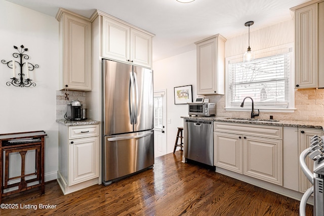 kitchen featuring decorative light fixtures, stainless steel appliances, dark wood-type flooring, a sink, and light stone countertops