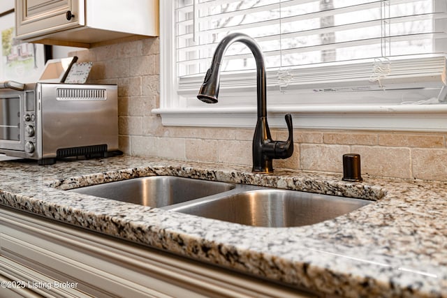 interior details with stone counters, a toaster, a sink, and backsplash