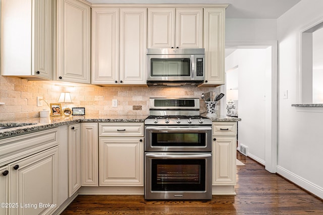 kitchen featuring visible vents, decorative backsplash, appliances with stainless steel finishes, light stone counters, and cream cabinetry