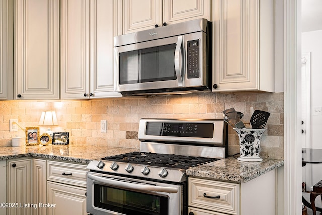 kitchen with light stone countertops, cream cabinetry, stainless steel appliances, and backsplash