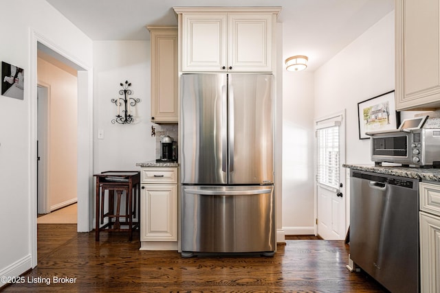 kitchen with stainless steel appliances, cream cabinetry, dark wood-type flooring, and stone countertops