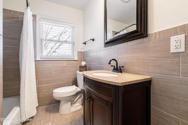 full bath with toilet, a wainscoted wall, wood finished floors, vanity, and tile walls