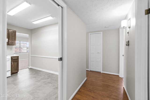 hallway featuring a textured ceiling, wood finished floors, and baseboards