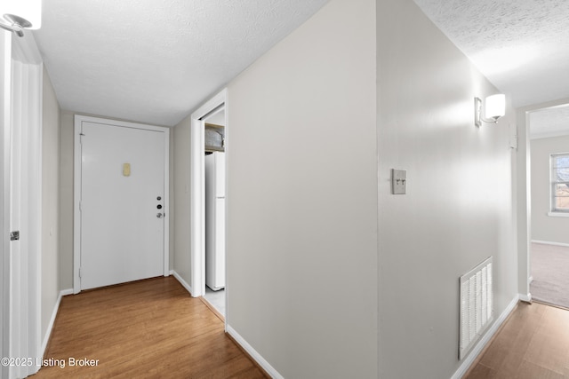 corridor featuring visible vents, a textured ceiling, and wood finished floors