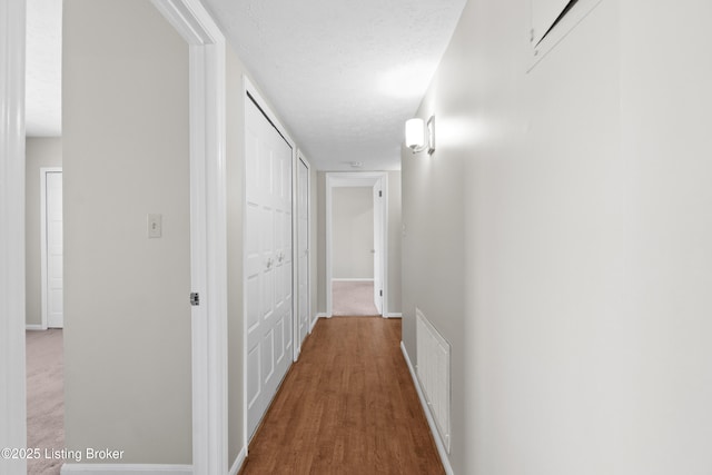 hallway featuring visible vents, a textured ceiling, baseboards, and wood finished floors