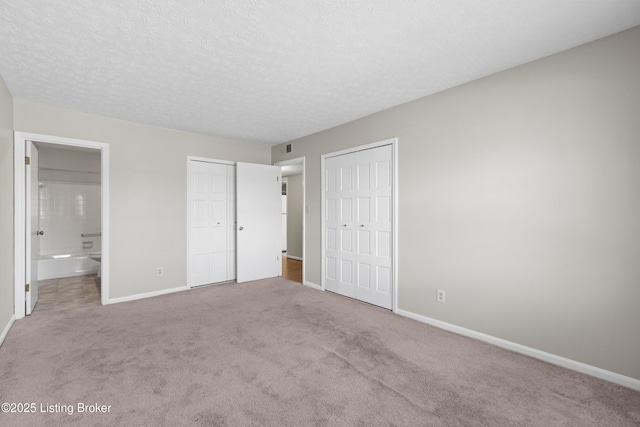 unfurnished bedroom featuring baseboards, connected bathroom, a textured ceiling, carpet floors, and two closets