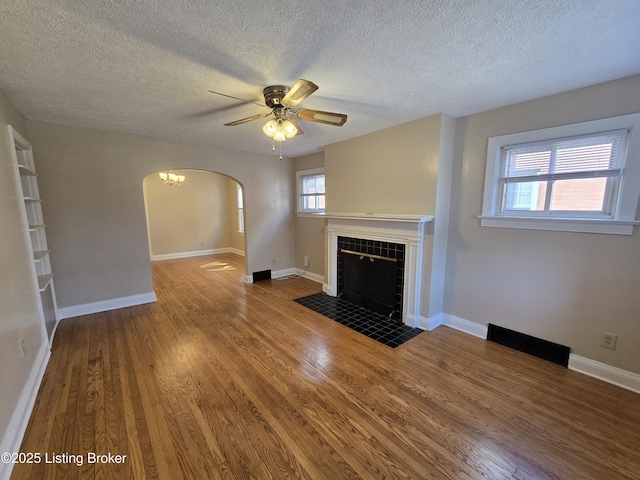 unfurnished living room featuring baseboards, arched walkways, wood finished floors, and a tile fireplace