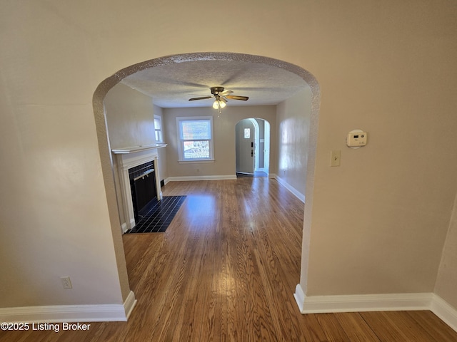 unfurnished living room with a fireplace with flush hearth, a textured ceiling, baseboards, and wood finished floors