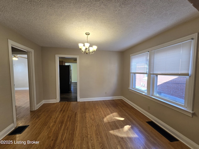 unfurnished dining area with dark wood-type flooring, visible vents, a notable chandelier, and baseboards