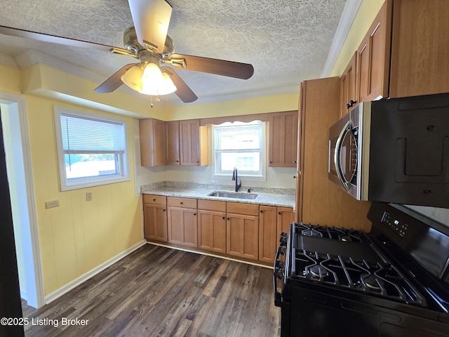 kitchen with black gas range, dark wood-style flooring, a sink, brown cabinetry, and stainless steel microwave