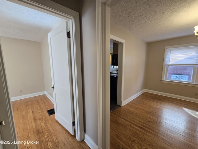 hall with baseboards, visible vents, light wood-style flooring, and a textured ceiling