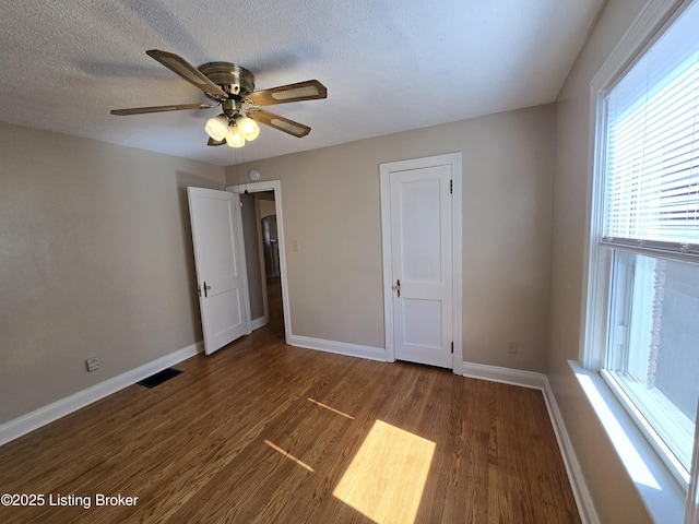 unfurnished bedroom with baseboards, visible vents, ceiling fan, dark wood-style flooring, and a textured ceiling