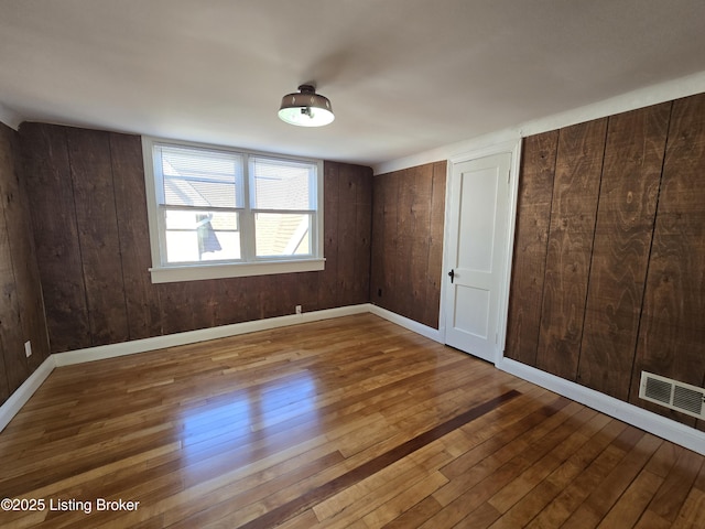 unfurnished bedroom featuring multiple closets, visible vents, wooden walls, baseboards, and hardwood / wood-style flooring