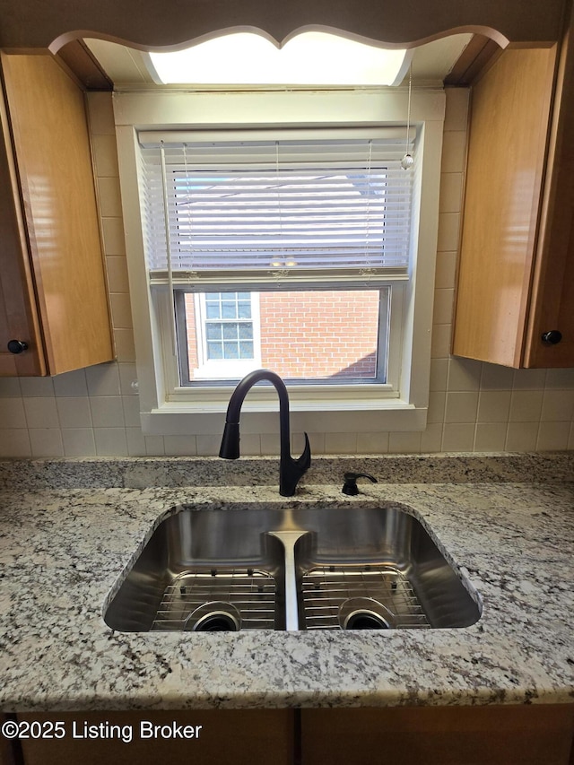 details with light stone counters, backsplash, a sink, and brown cabinets