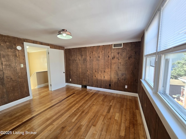 spare room featuring light wood finished floors, wood walls, visible vents, and baseboards