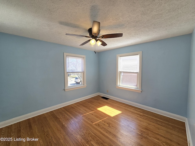 empty room featuring visible vents, a ceiling fan, a textured ceiling, wood finished floors, and baseboards