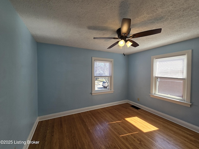 spare room featuring baseboards, visible vents, ceiling fan, wood finished floors, and a textured ceiling