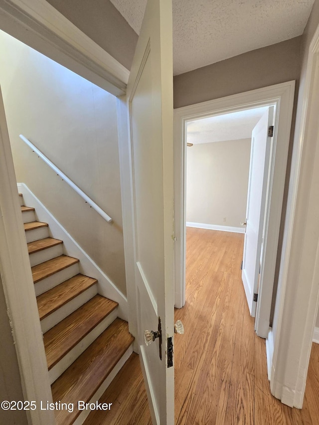 stairs featuring a textured ceiling, wood finished floors, and baseboards