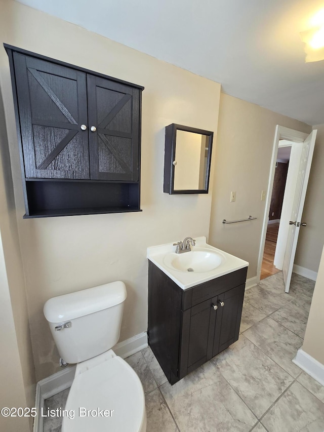 half bathroom featuring marble finish floor, baseboards, vanity, and toilet